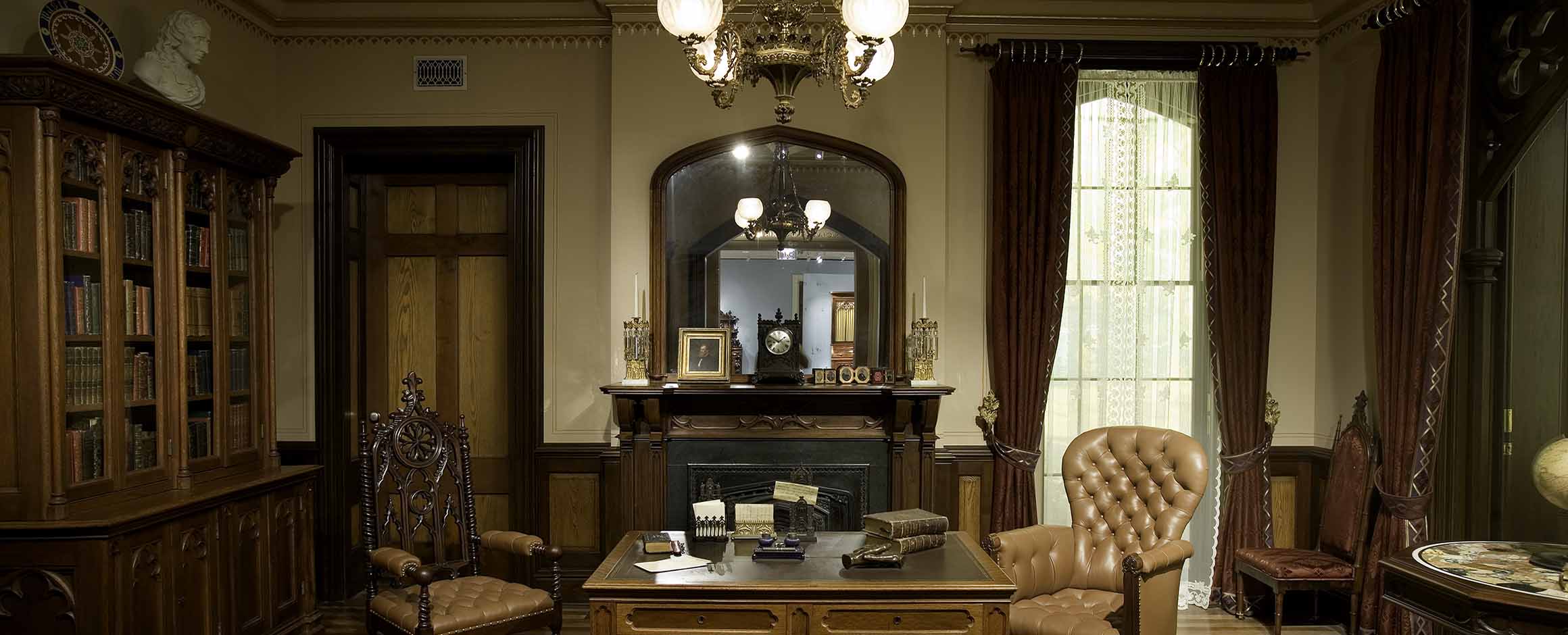 The desk in the Gothic Revival Library in front of the fireplace and looking glass