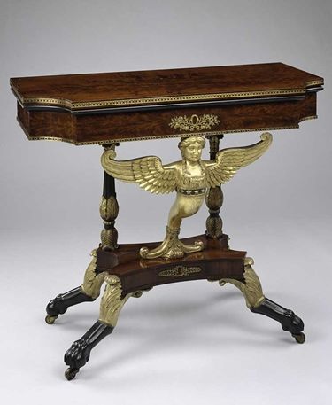 A wooden claw foot card table with an extragagent golden embellishment of a winged woman
