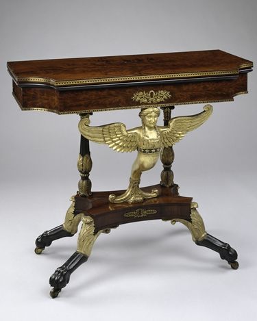 Photograph of a wooden card table on clawfoot wheels with a golden embellishment of an angel.
