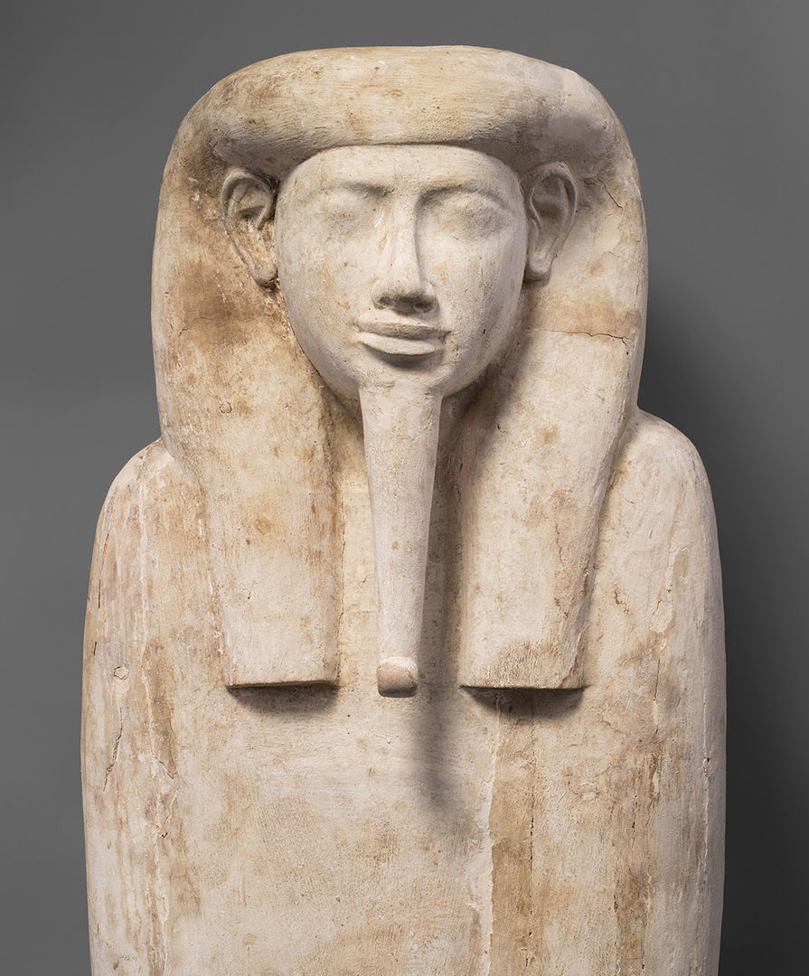 Top part of a whitewashed coffin in the form of a mummy, with a long curled beard and a long wig.
