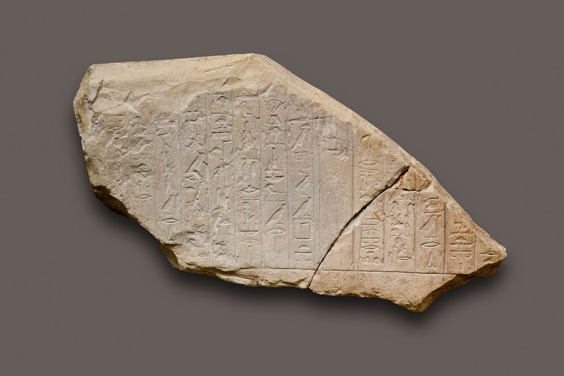 A large fragment of whitish-brown stone, cracked on one side, with columns of hieroglyphs carved into its surface.