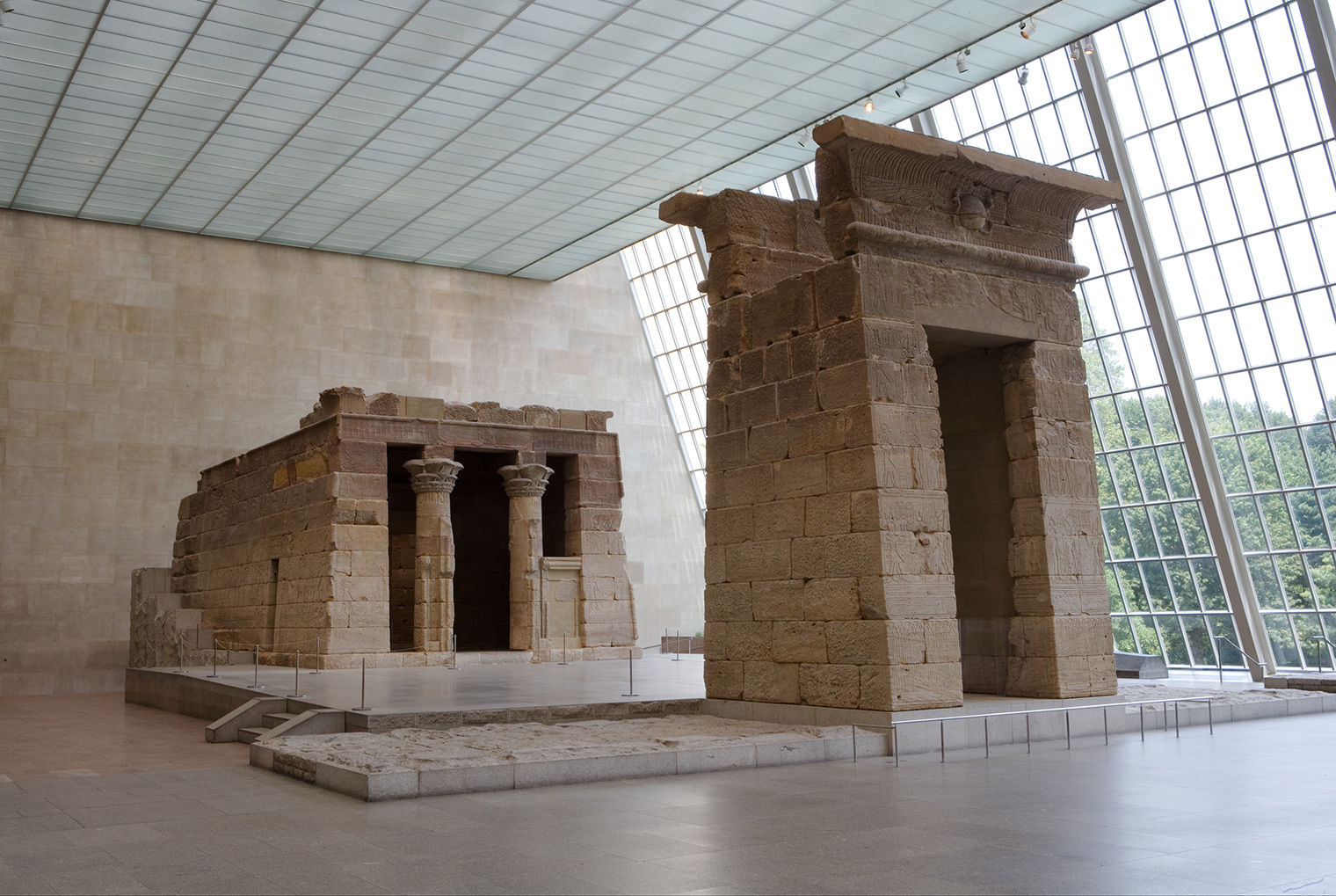 A view of the Temple of Dendur, with the tall narrow gateway in the foreground, and the square temple in the back, looking toward a wall of windows