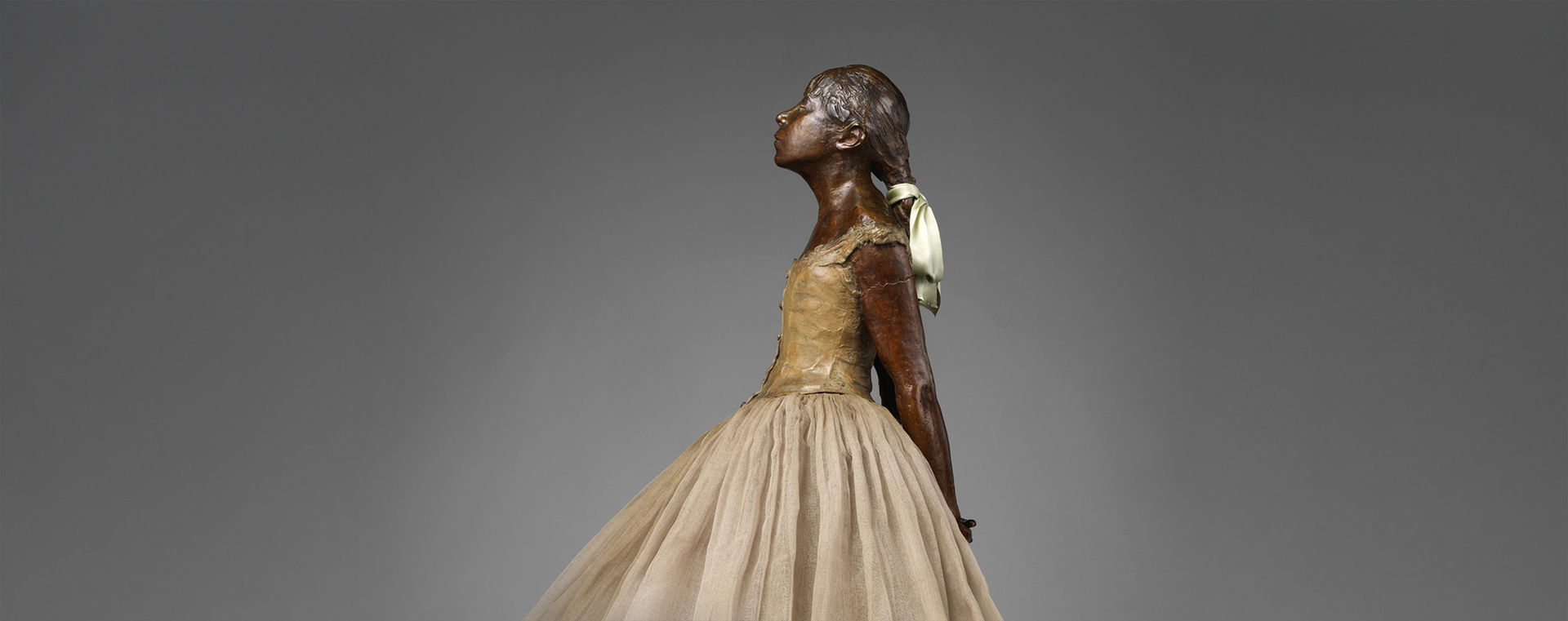 Detail of Degas bronze sculpture showing young girl in ballet dress gazing upward, her hair tied back with a satin ribbon.