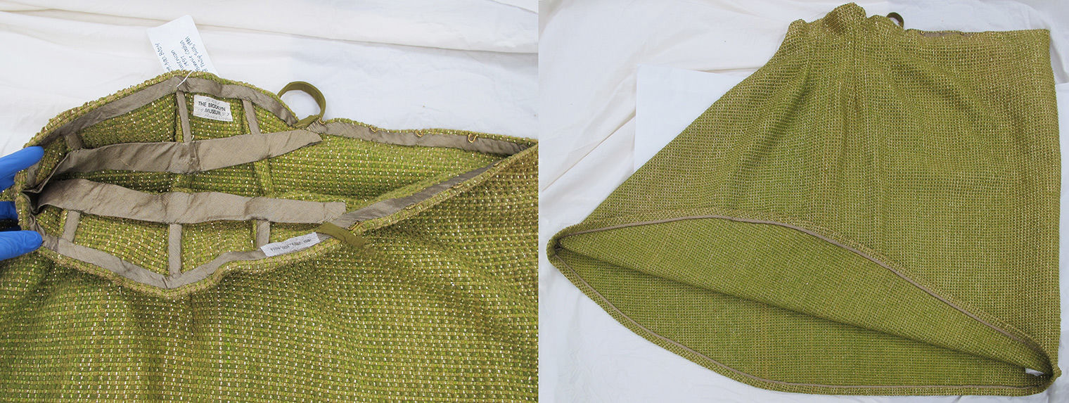 At left, an interior view of the green skirt’s waistline and center back closure, which is finished with a narrow taupe bias tape. The waist and hip areas are shaped by three darts per side, each of which is stiffened by a piece of boning encased in a taupe bias tape channel. A waist stay is sewn into the center front of the skirt and tacked to each of the six bones. The back ends of the waist stay are secured beneath the bias tape that edges the waistline. At right, the green skirt is laid flat on a table with the bias-cut center front seam towards the left and the center back fold on the right. The hem is turned up to show a one-and-a-half-inch seam allowance with the cut edge bound with taupe bias tape. 