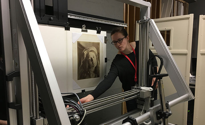 The conservator, Louisa Smieska, adjusts a large piece of scanning equipment in front of a mounted photograph by Julia Margaret Cameron