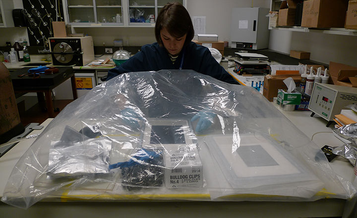 Conservator reaching in under plastic dome, examining sealed packages for autochromes.