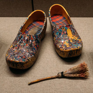 A pair of clogs spattered with colorful paint in a display case with a straw brush