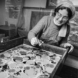 Black-and-white photograph of Peggy Skycraft marbling paper in her studio 