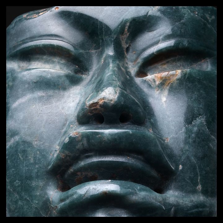 A close-up of a dark-green stone sculpture's face