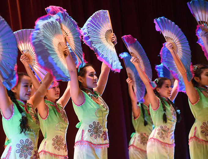 Young women in colorful Asian-inspired costumes dancing with large, colorful folding fans