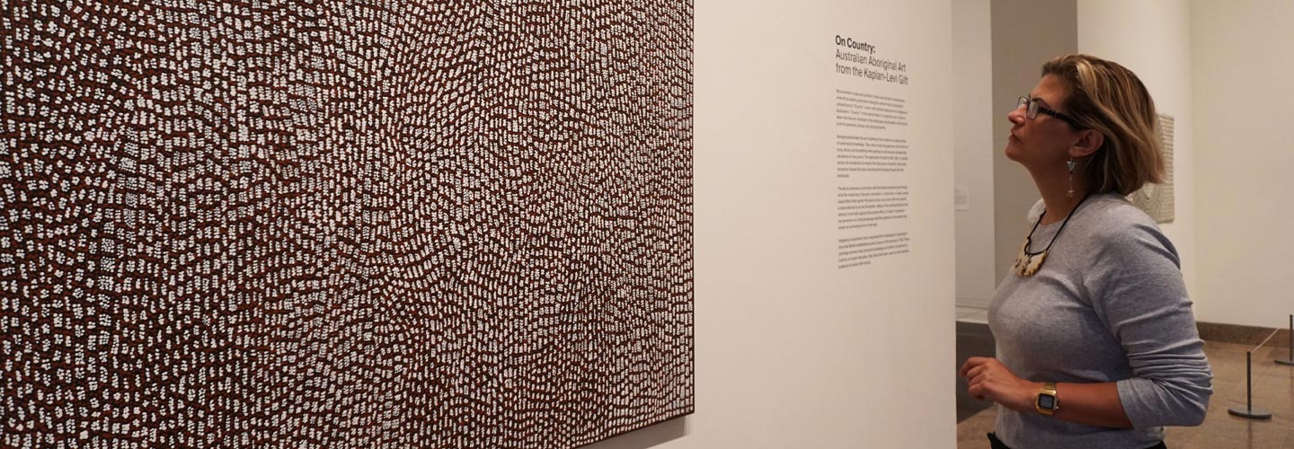 Curator Maia Nuku stands in front of a painting in an exhibition gallery