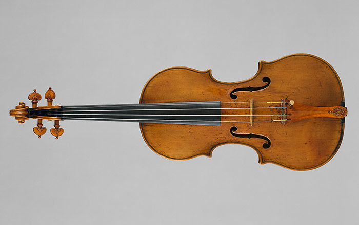 A sixteenth-century violin, with fleurs-de-lis tuners, laid down on a gray background