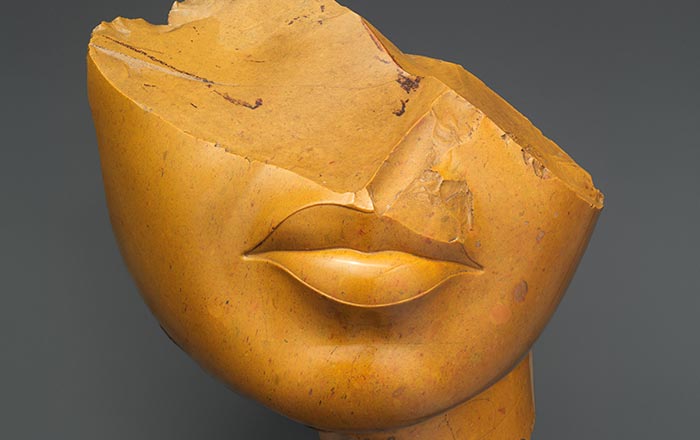 Fragment of a Queen's Face made out of yellow jasper. Only the bottom half of her face, her lips and chin are discernible. 
