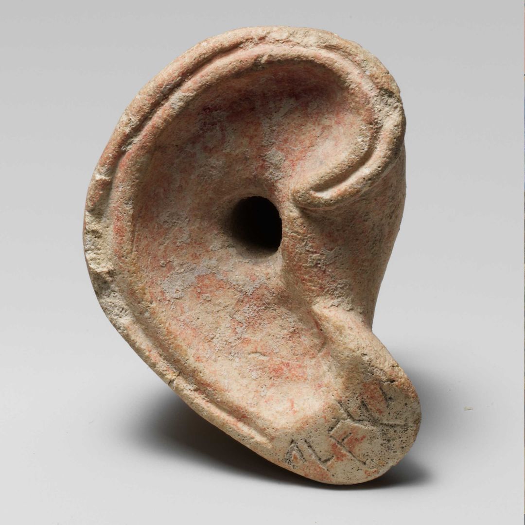 Sculpture of a right ear with the canal indicated by a circular hole, traces of red paint, and five syllabic signs carved into the lobe