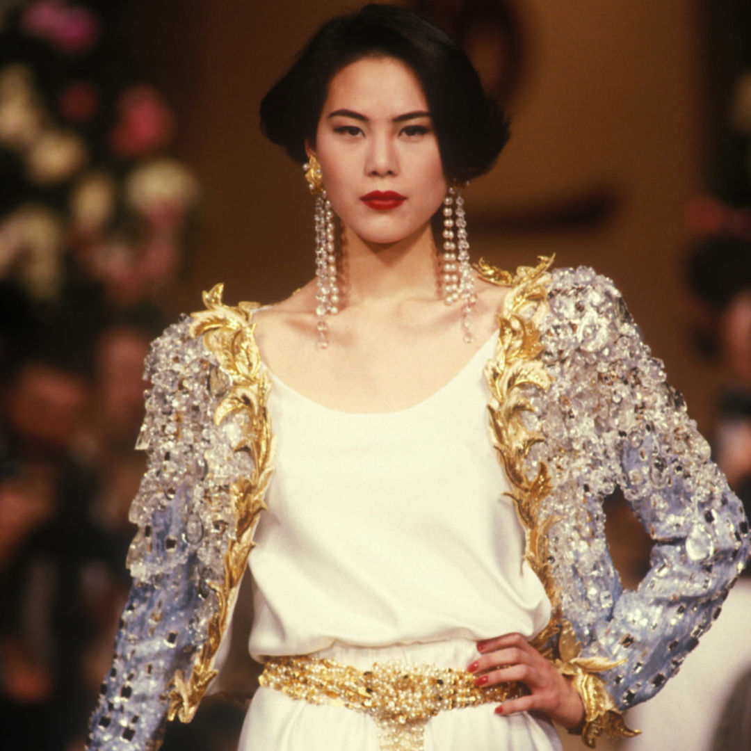 Model wearing a white silky outfit and a silver and gold embroidered jacket designed by Yves Saint Laurent