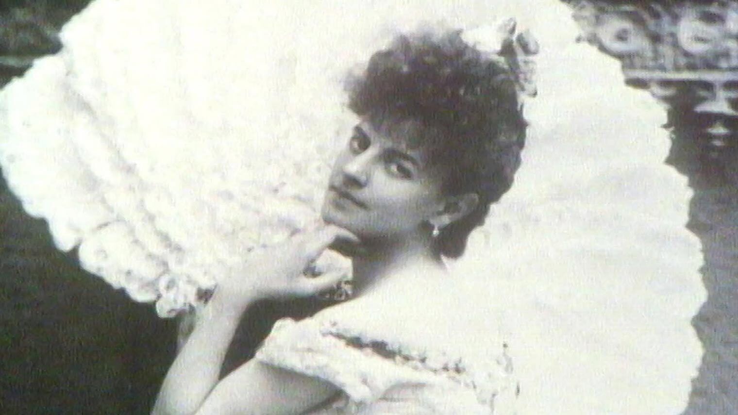 An old photo of an elegant woman wearing a white dress