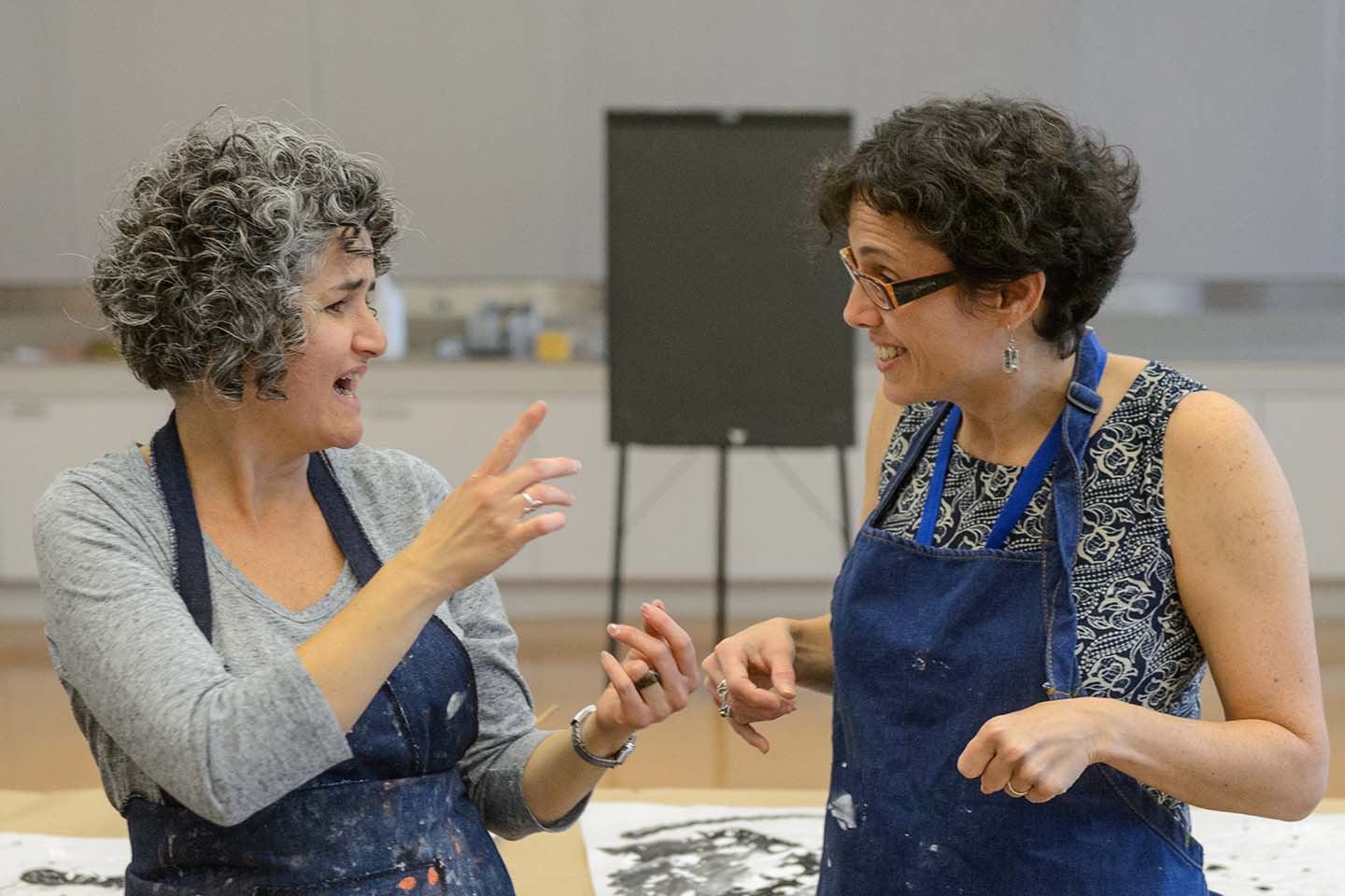 Two women wearing smocks for art-making communicating in American Sign Language