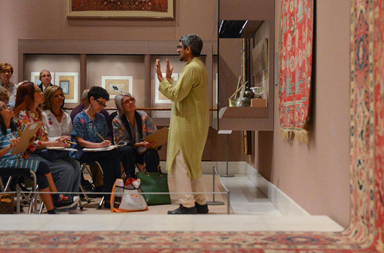 A curator standing in the Islamic galleries at The Met speaks to a seated crowd