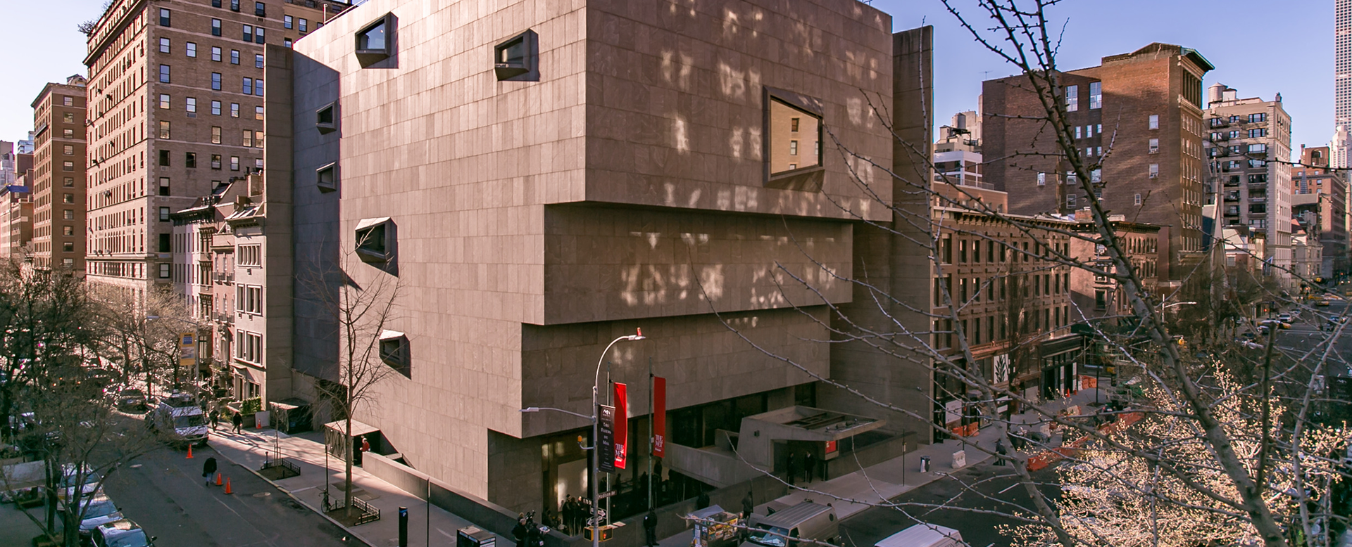 The Met Breuer in the daytime on a sunny cloudless day. The building is an inverted pyramid made of concrete.