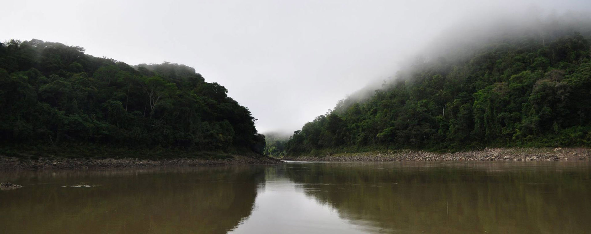 Smooth river between two green hills in the fog
