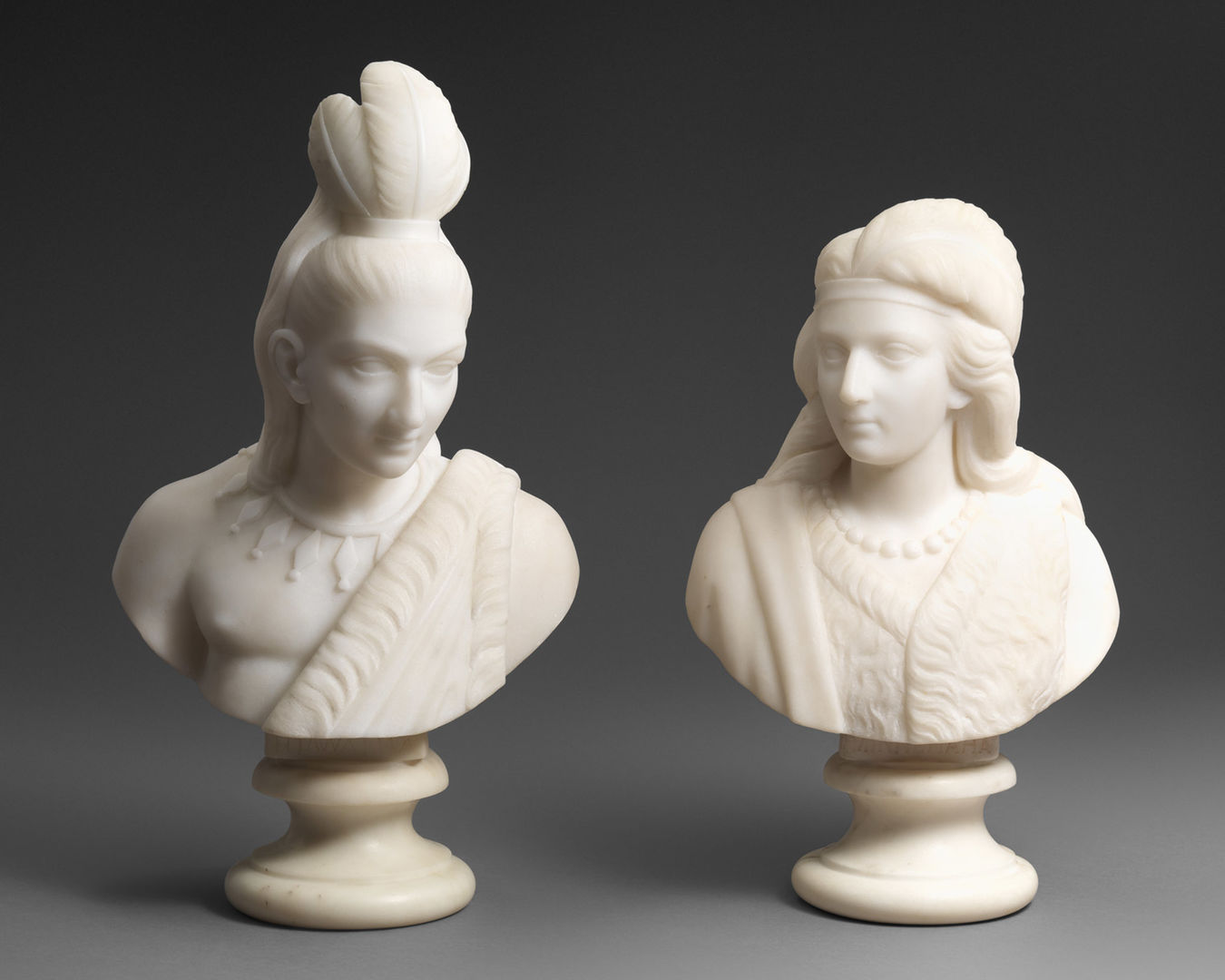 Two sculptural busts, one of a man and the other a woman, both wearing Indigenous dress