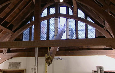 Video still of workers maneuvering a beam through an open window.