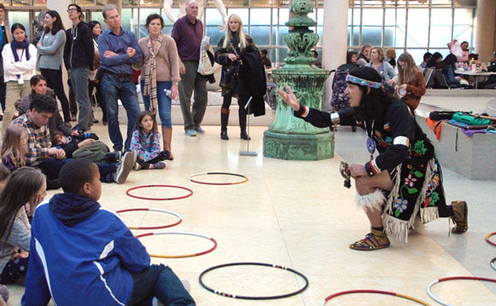 Ty Defoe wearing traditional Native American garment tells a story to a group of people