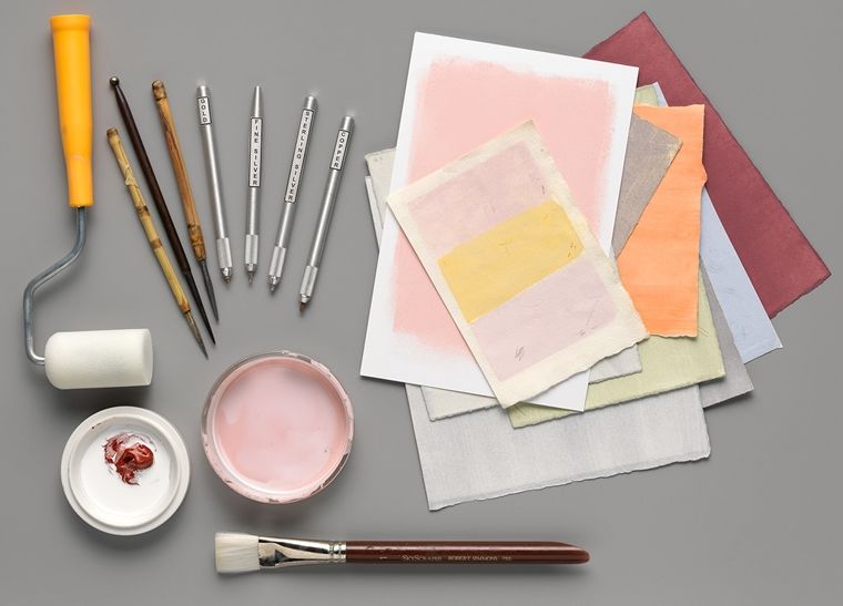 An artful arrangement of specialized tools for making metalpoint drawings beside a stack of colorful paper.