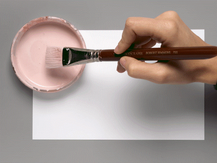 A moving image of a brush dipping into pink pigment and spreading it on a white sheet of paper.