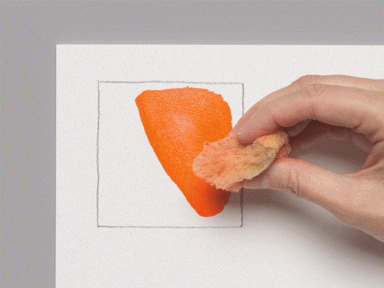 A moving image of large orange  watercolor mark being on a spiral-ring notebook page with a sponge, then overlayed with purple marks and partially removed with a blade.