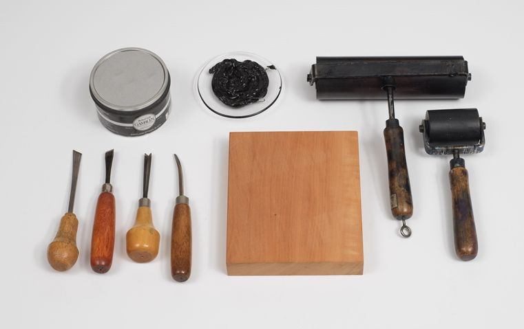 Photo of woodcutting tools, including a block, chisel, gouche, knife, ink ball, roller, and ink