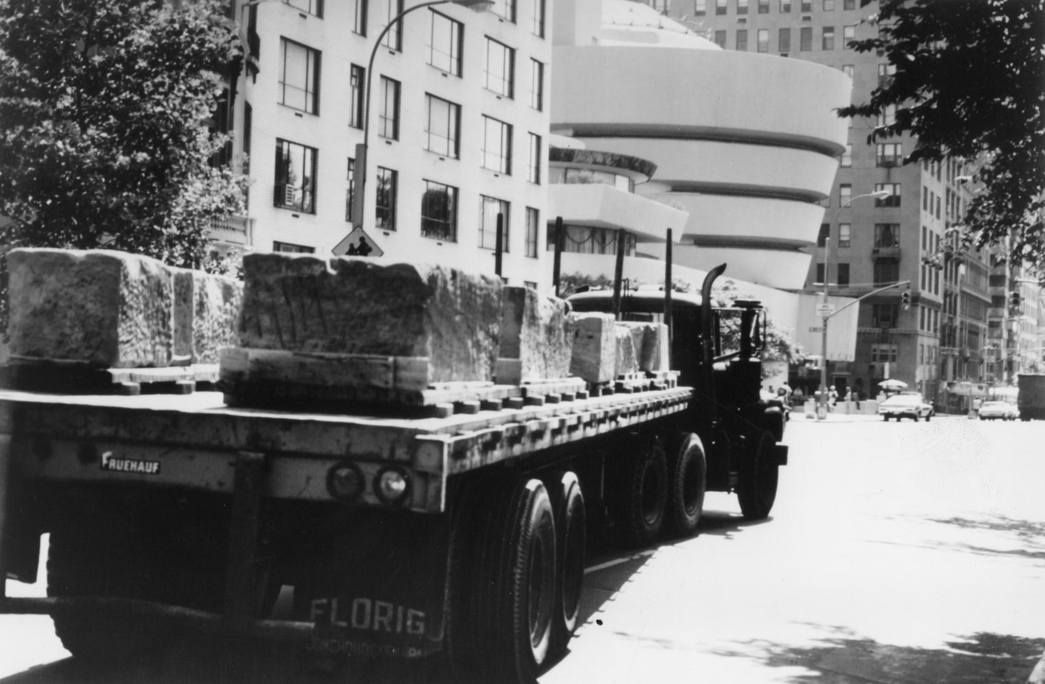 Blocks of the Temple of Dendur being driven down Fifth Avenue on the backs of trucks and passing along the Guggenheim Museum 