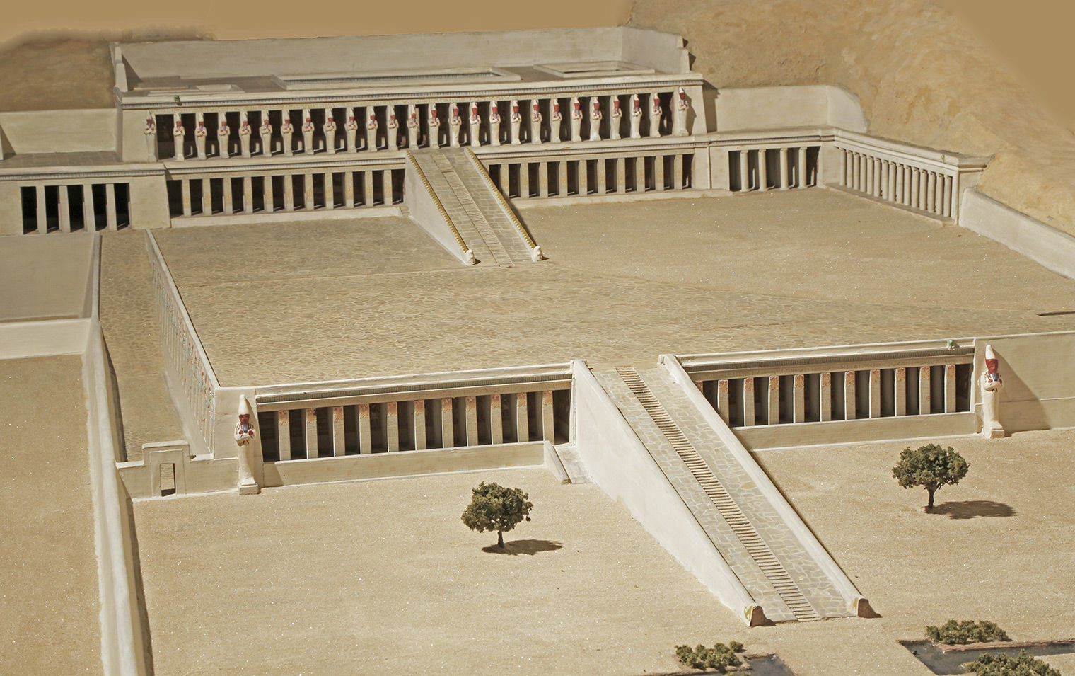 Terraced temple with ramps, all beige in a sandy landscape, with mummiform statues on the main levels.