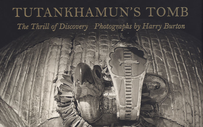 The top part of a book cover, with the title, Tutankhamun's Tomb, The Thrill of Discovery, Photographs by Harry Burton. Below is the upper part of the head of a coffin, with figures of a vulture and cobra attached.