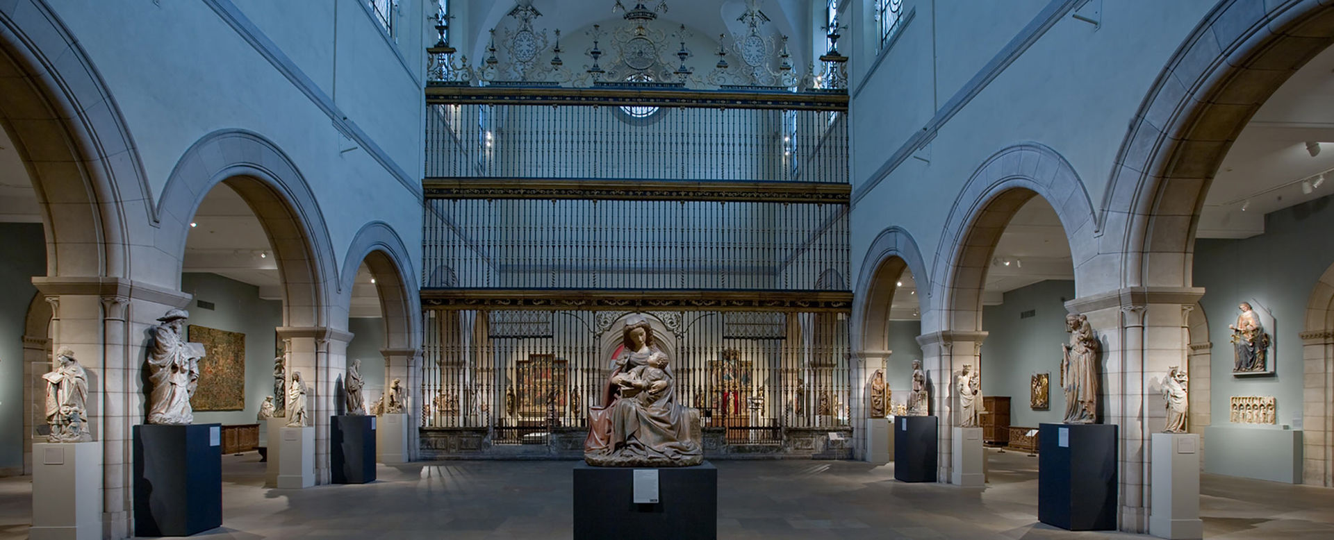 A very large gallery with a dark stone floor and central arcades subdividing the space for medieval Christian sculptures and church pieces.