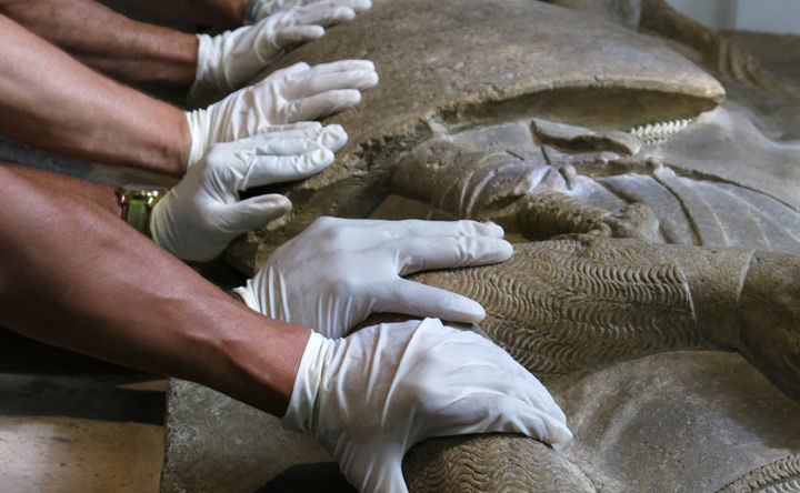 Five gloved hands touch a sculpture. 