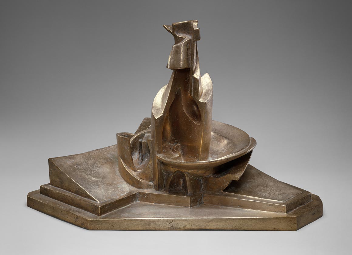 A bronze sculpture by Umberto Boccioni from 1913 (cast in 1950) titled "Development of a Bottle in Space." The work resembles a fountain with a central, vertical form hugged on the bottom half by curved shapes on the left and right. This central, vertical form rises from a shallow, curved plate. The central form and curved plate are placed on a trapezoidal stand accentuated by a triangular shape on the left. Although the material is made of hard bronze, the curves of the central form and plate as well as the diagonal lines of the stand invigorate the work.