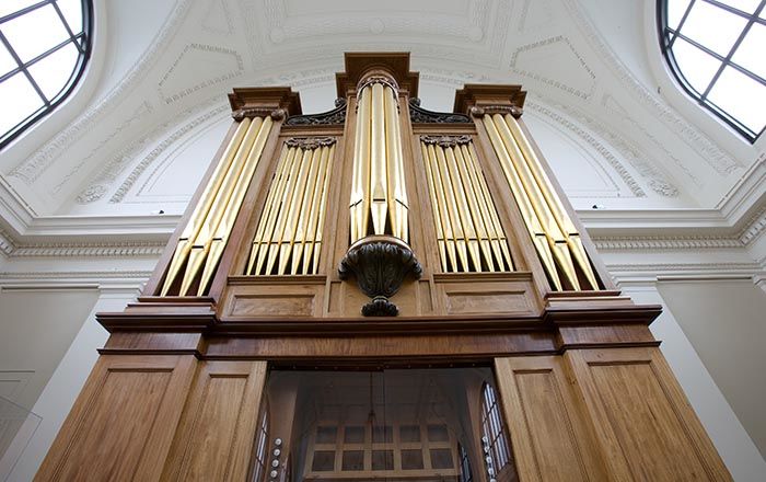 A close-up view looking up at a huge brass pipe organ in a brightly lit gallery with a high, vaulted ceiling