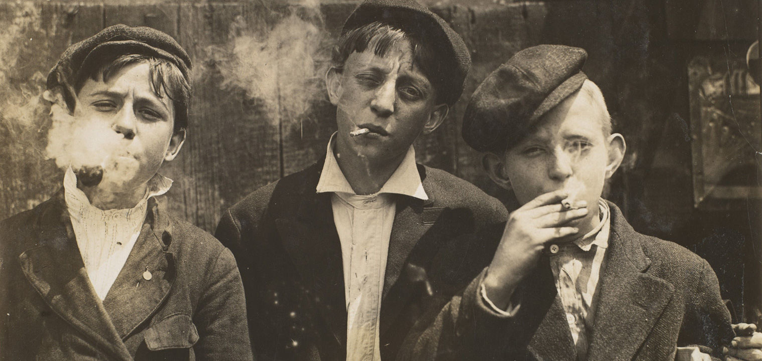 Archival image of three newsies smoking cigarettes in 1910