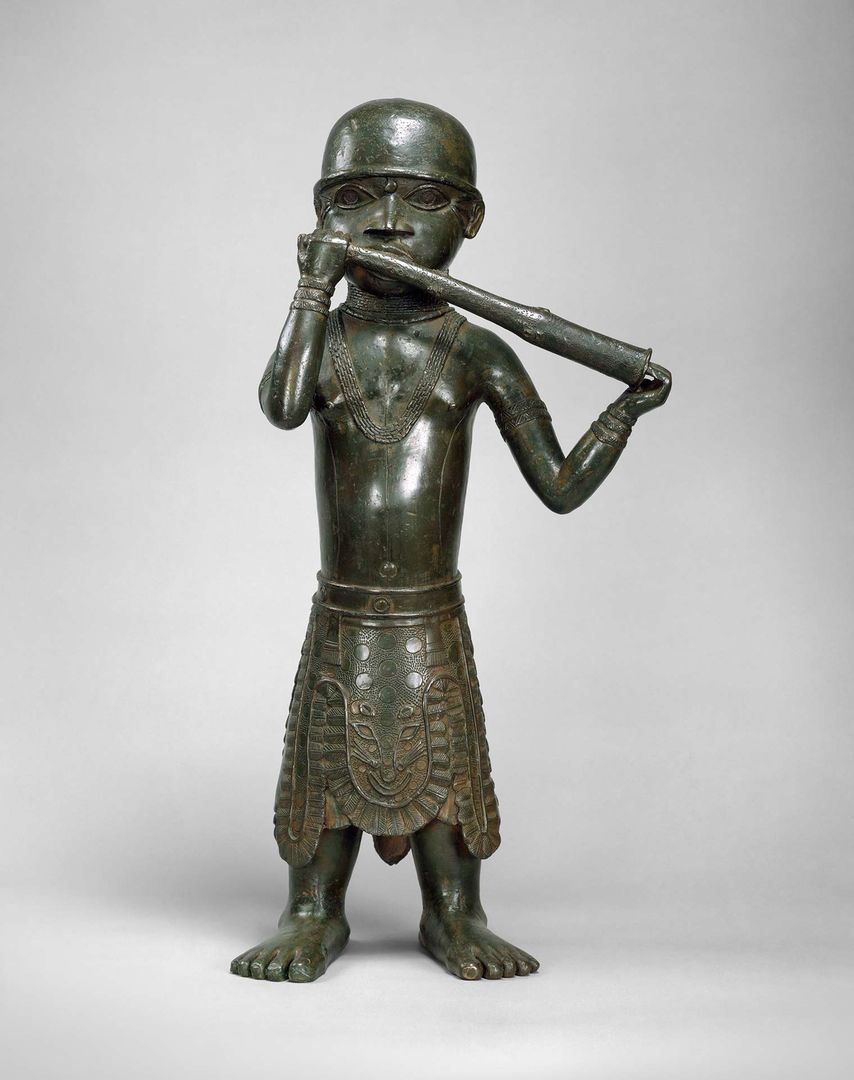 A medium-sized brass sculpture of a man in traditional Edo dress playing a horn.