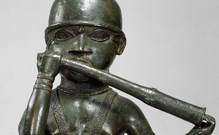 Detail of a Nigerian sculpture, made of dark brass with a green patina and standing two feet tall, of a man playing a horn