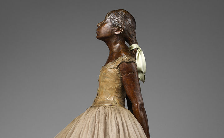 Detail of Degas bronze sculpture showing young girl in ballet dress gazing upward, her hair tied back with a satin ribbon.