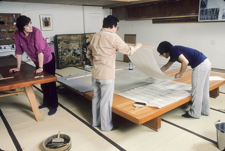 Three conservators applying a kozo paper lining to a scroll mounting silk