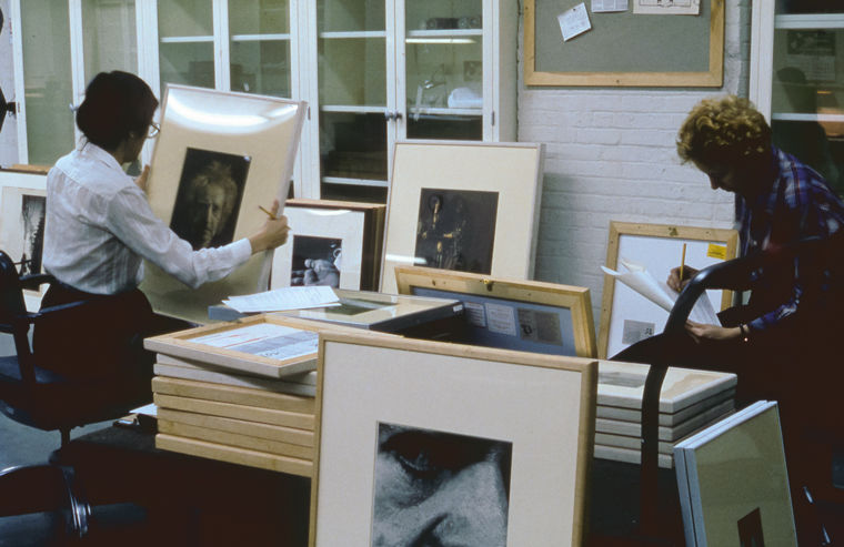 Man and woman in an office looking over stacks of framed artworks, checking off list