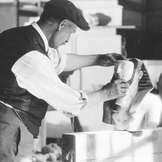 Black-and-white archival photo of man fitting a face to an Egyptian statue.