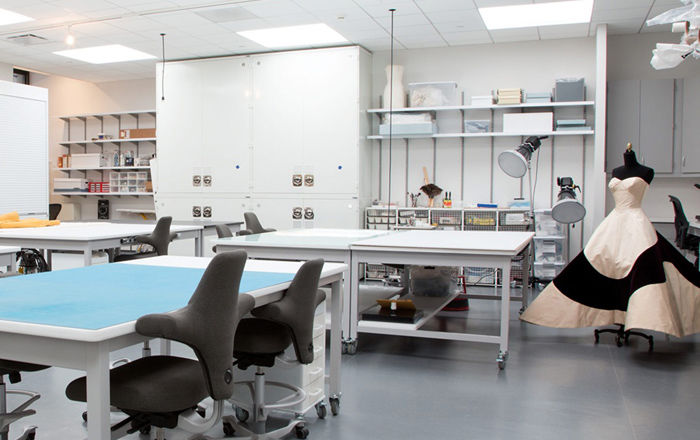 View of the Costume Institute Conservation lab, showing various examination tables, shelves of instruments, and a Charles James couture ballgown in the corner