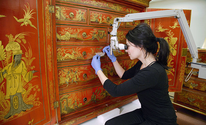 Met fellow looks through microscope at red lacquer cabinet