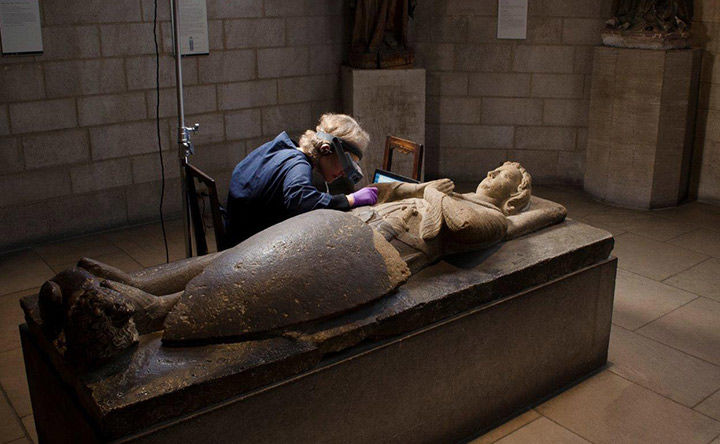 An objects conservator working on a medieval sarcophagus in the shape of a human figure with a shield