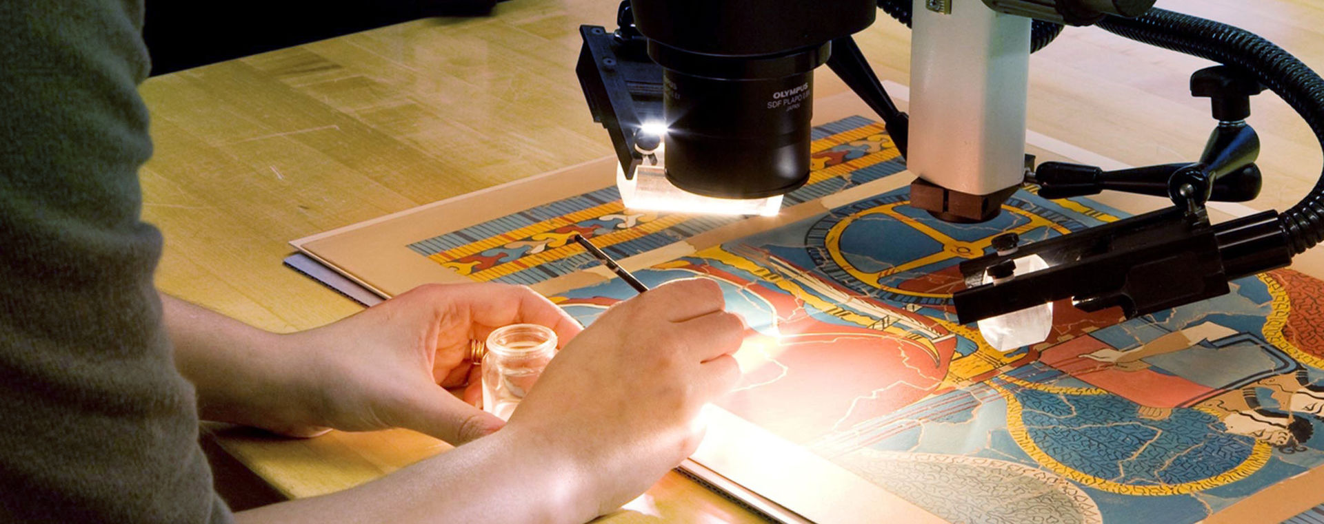 A woman looking through a telescope, examining a colorful work of art on paper