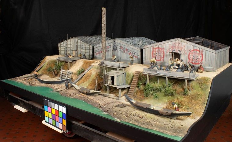 Miniature diorama of a Kwakwaka'wakw village with three buildings, three canoes, and a number of small figurines.